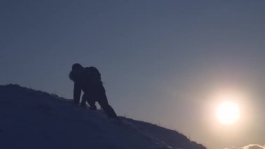 Erkek için güneş kışın ayarlama parlama içinde karlı dağın tepesine tırmanma silüeti. Gezgin karlı dağlarda alanı keşfetmek. Kavramı, yalnız çalışırım. Zafer, zirve fethetmek