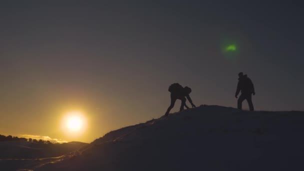 歓喜の登山者のシルエットには、両手を上げて、夕日のまぶしさに高い雪の山を征服した後の幸せからジャンプが発生します。観光客で山に旅行します。チームワークの概念 — ストック動画