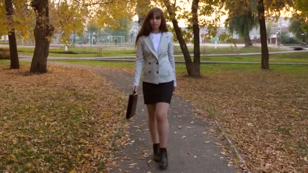 Девушка-адвокат с черным портфелем идет дорожкой в осенний парк — стоковое видео