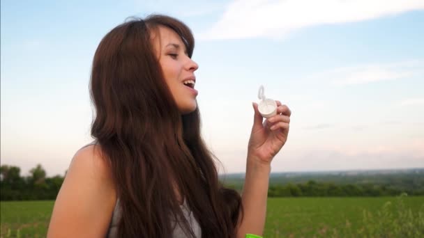 Happy girl with long hair blows out transparent soap bubbles against the blue sky and smiles. Slow motion. — Stock Video