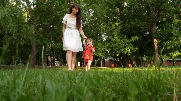 Enfant et mère marcher sur herbe verte pelouse dans le parc de la ville d'été et souriant . — Photo