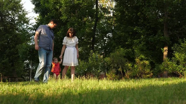 Baby Mama i tata są chodzą trzymając się za ręce i grając w parku miejskim na trawa trawnik. — Zdjęcie stockowe
