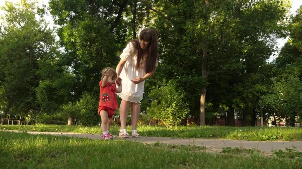 Maman et petite fille marchent le long du chemin dans le parc d'été. babys premiers pas avec maman — Photo