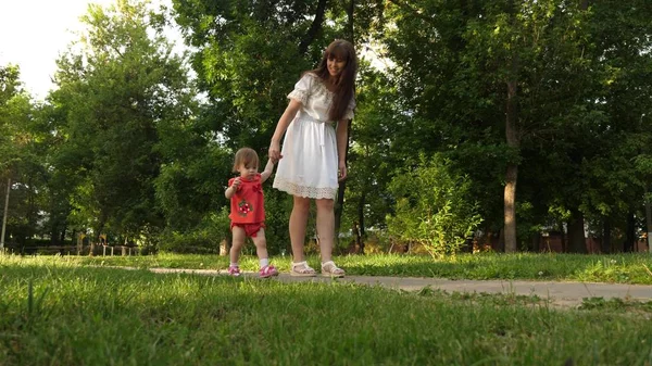 Ibu dan putri kecil berjalan di sepanjang jalan di taman musim panas. babys langkah pertama dengan ibu — Stok Foto