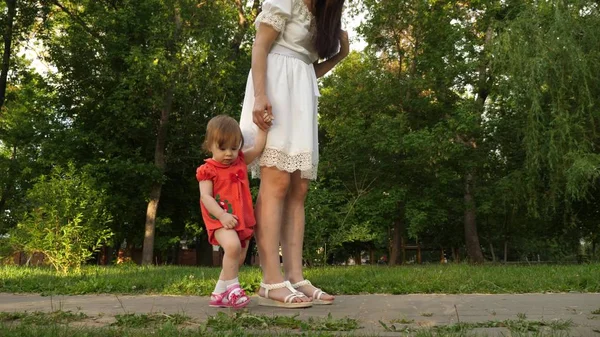 Mom and little daughter are walking along path in the summer park. babys first steps with mom
