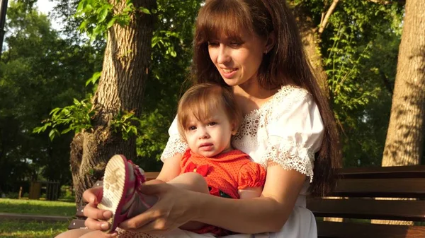 Mutter Schuhe Kinderschuhe sitzt auf Bank im Sommerpark und lächelt. Zeitlupe — Stockfoto