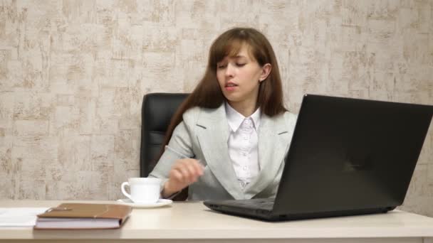 Mooi meisje zittend in de stoel in kantoor en typen op laptop en drinken koffie uit witte kop. jonge vrouw zakenvrouw werkt op computer. meisje is chatten op een laptop — Stockvideo