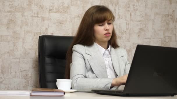 Красивая девушка сидит в кресле в офисе и печатает на ноутбуке. молодая деловая женщина, работающая за компьютером. Девушка болтает на ноутбуке — стоковое видео