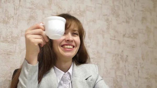 Menina bonita senta-se na cadeira no escritório falando e bebendo café da xícara branca. jovem empresária está descansando e bebendo chá no local de trabalho . — Fotografia de Stock