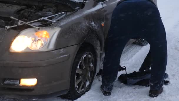 Человек Поднимает Домкрат Автомобиль Сломался Заснеженной Дороге — стоковое видео