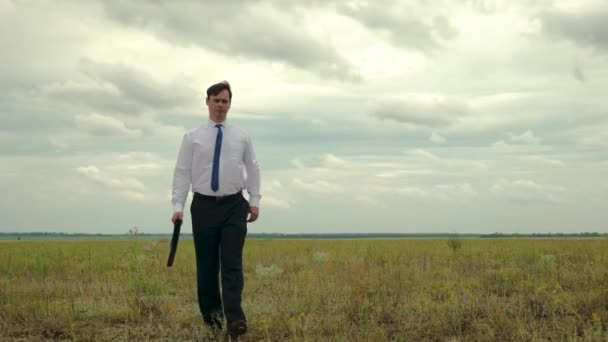 Agrónomo cruza el campo. hombre de negocios con camisa blanca y corbata azul lleva en la mano un maletín negro con documentos . — Vídeos de Stock