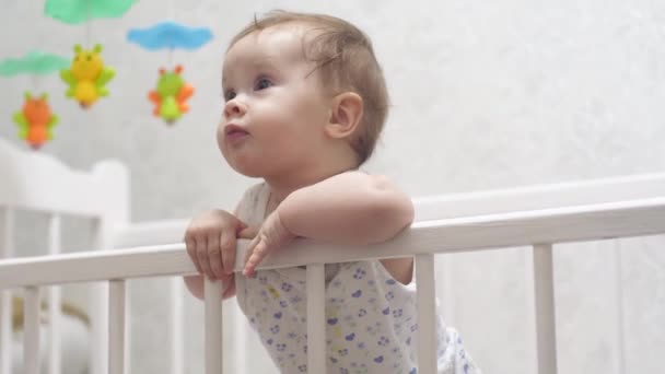 Ευτυχισμένο παιδί στέκεται στα πόδια του σε παιδικό κρεβάτι. γέλια μωρών — Αρχείο Βίντεο