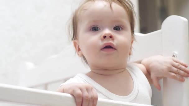 Bebê segura a borda da cama do bebê . — Vídeo de Stock