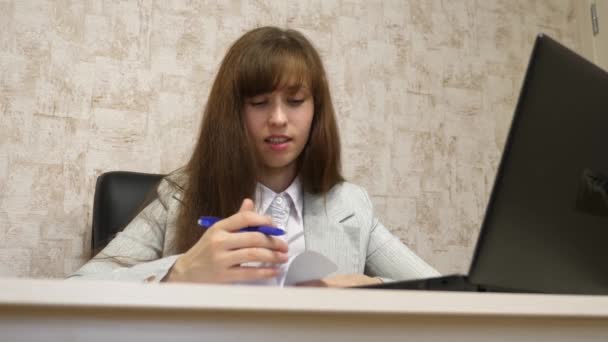 Όμορφη κοπέλα, κάθεται σε μια καρέκλα στο γραφείο και μιλάμε και λήψη σημειώνει στην bloknot. νεαρή γυναίκα επιχειρηματίας εργάζονται με έναν πελάτη σε ένα γραφείο — Αρχείο Βίντεο