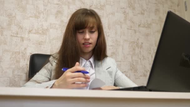 Hermosa chica sentada en una silla en la oficina y hablando y tomando notas en bloknot. joven empresaria que trabaja con un cliente en una oficina — Vídeos de Stock