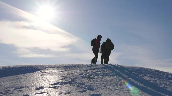 Três alpenistas escalam corda na montanha nevada. Turistas trabalham juntos como equipe balançando alturas superando dificuldades. silhuetas de viajantes sobem à sua vitória colina acima no gelo em raios do sol . — Fotografia de Stock
