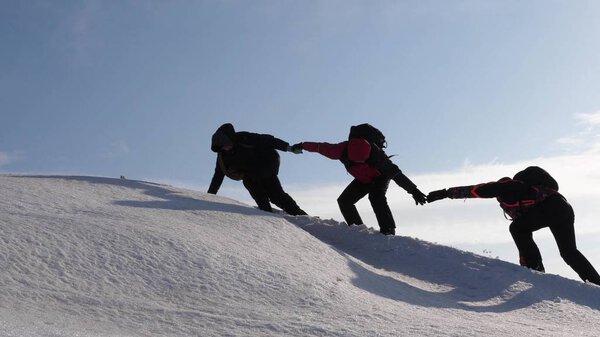 climbers hand in hand climb to top of a snowy mountain. the team of travelers in winter go to their goal of overcoming difficulties. well-coordinated teamwork tourism.