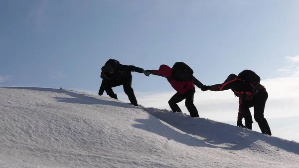 登山者は、雪に覆われた山の頂上に登りを手で手します。冬の旅行者のチームは、困難を克服するための自分の目標に行きます。見事な連携観光. — ストック写真