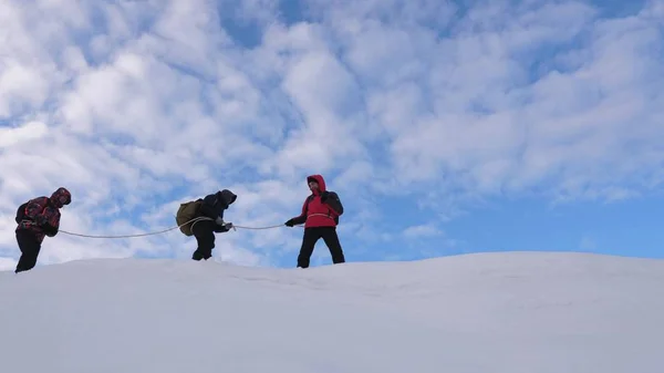 Альпинисты, связанные верёвкой, следуют друг за другом вдоль снежного хребта. Команда путешественников зимой поднимается на вершину горы. хорошо скоординированный командный туризм зимой — стоковое фото
