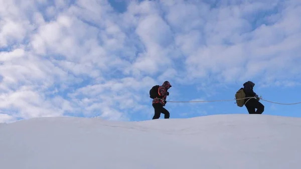 Mit Seilen gebundene Bergsteiger folgen einander entlang des schneebedeckten Grats. Team von Reisenden im Winter auf den Gipfel des Berges zu gehen. Gut koordinierter Teamwork-Tourismus im Winter — Stockfoto