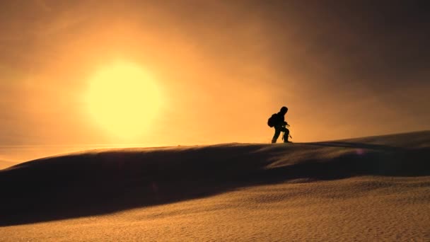 Fotógrafo viajante no inverno vai em cume nevado em raios de pôr-do-sol amarelo. montanhista com câmera e tripé está andando na neve ao longo do topo de um holom . — Vídeo de Stock