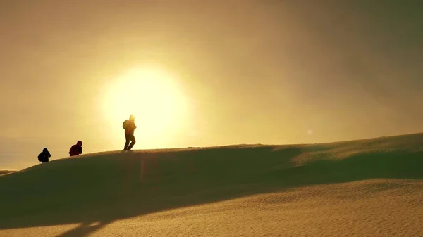 Team of travelers follow each other along snow ridge against backdrop of yellow sunset. coordinated teamwork of tourists in the winter. teamwork of people in difficult conditions. — Stock Photo, Image