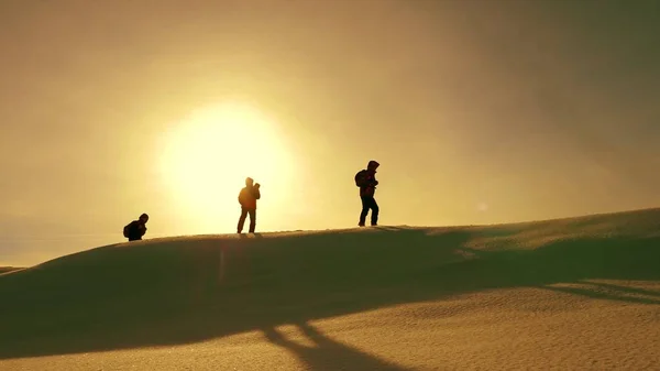 Team of travelers follow each other along snow ridge against backdrop of yellow sunset. coordinated teamwork of tourists in the winter. teamwork of people in difficult conditions. — Stock Photo, Image