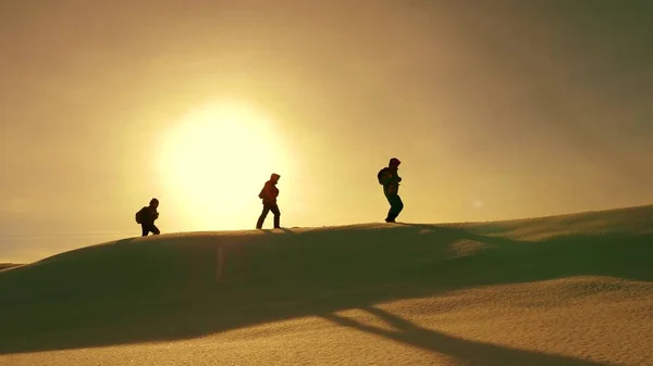 Team of travelers follow each other along snow ridge against backdrop of yellow sunset. coordinated teamwork of tourists in the winter. teamwork of people in difficult conditions. — Stock Photo, Image