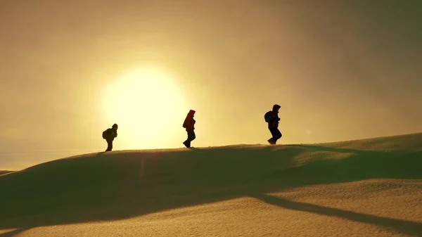 Team of travelers follow each other along snow ridge against backdrop of yellow sunset. coordinated teamwork of tourists in the winter. teamwork of people in difficult conditions. — Stock Photo, Image