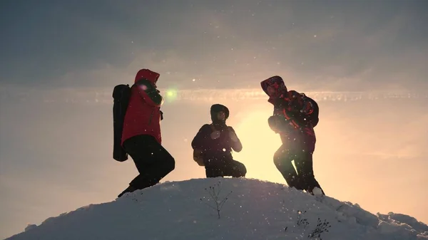 Trabajo en equipo y victoria. Los turistas llegan a la cima de la colina nevada y se regocijan por la victoria contra el telón de fondo de una puesta de sol amarilla. Trabajo en equipo de personas en condiciones difíciles . —  Fotos de Stock