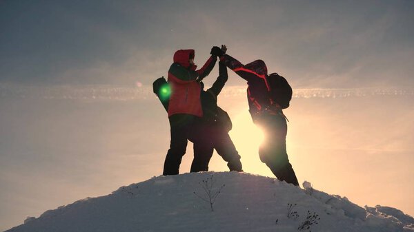 team work and victory. Tourists come to top of snowy hill and rejoice at victory against backdrop of a yellow sunset. teamwork of people in difficult conditions.