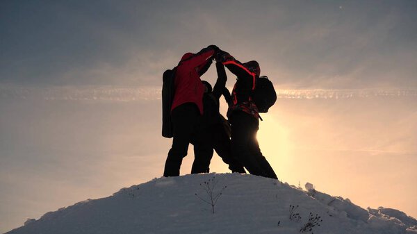 team work and victory. Tourists come to top of snowy hill and rejoice at victory against backdrop of a yellow sunset. teamwork of people in difficult conditions.