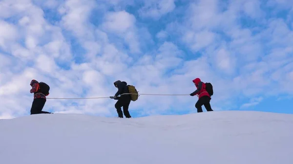 Ορειβάτες πάνε μαζί μετά από φίλο κατά μήκος τη χιονισμένη κορυφογραμμή. ομάδα ταξιδιώτες το χειμώνα πάει στην κορυφή του βουνού. καλά συντονισμένη ομαδική δουλειά τουρισμού το χειμώνα — Φωτογραφία Αρχείου