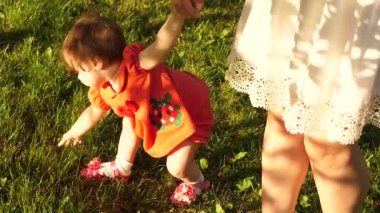 küçük kız elleri ile yeşil çim tatili ve elle annesini tutar. Anne ve küçük kızı baharda yeşil bir çim üzerinde yürüyor. mutlu çocukluk kavramı.