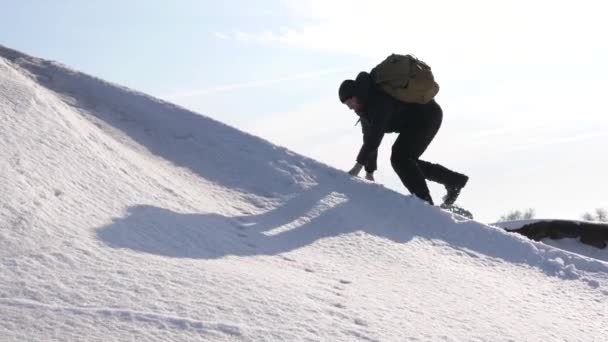 De man gaat naar de top naar zijn succes. Klimmer beklimt besneeuwde berg in stralen van felle zon. toerist maakt klim naar boven op de achtergrond van mooie lucht. — Stockvideo