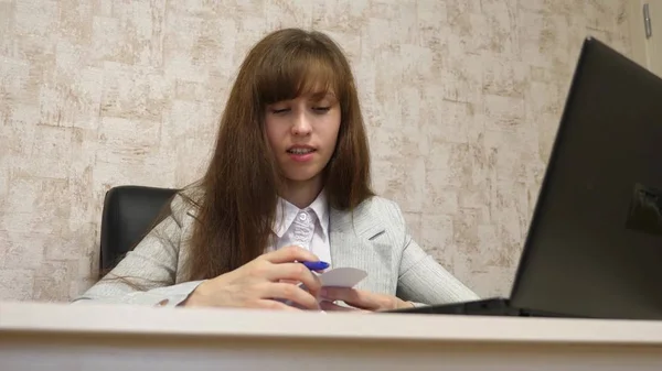 Красива дівчина сидить у кріслі в офісі, розмовляє і робить нотатки в блокноті. молода жінка-підприємець, що працює з клієнтом в офісі — стокове фото