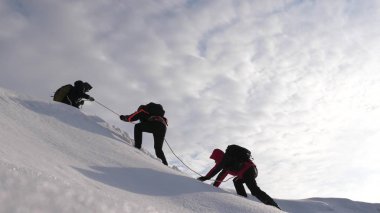 Travelers climb rope to their victory through snow uphill in a strong wind. tourists in winter work together as team overcoming difficulties. three Alpenists in winter climb rope on mountain. clipart