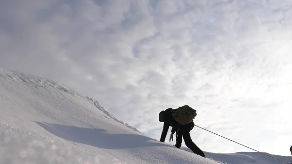 Путешественники поднимаются по канату к своей победе через снег в гору при сильном ветре. туристы зимой работают вместе, как команда преодоления трудностей. три альпиниста в зимнем альпинизме на гору . — стоковое фото