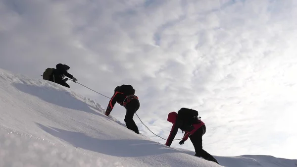 Travelers climb rope to their victory through snow uphill in a strong wind. tourists in winter work together as team overcoming difficulties. three Alpenists in winter climb rope on mountain. — Stock Photo, Image