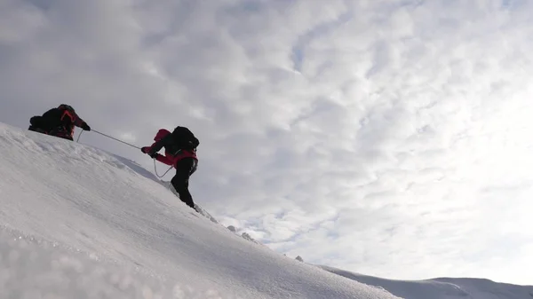Путешественники поднимаются по канату к своей победе через снег в гору при сильном ветре. туристы зимой работают вместе, как команда преодоления трудностей. три альпиниста в зимнем альпинизме на гору . — стоковое фото