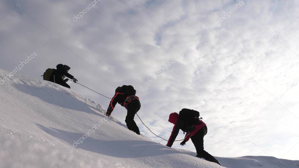 Travelers climb rope to their victory through snow uphill in a strong wind. tourists in winter work together as team overcoming difficulties. three Alpenists in winter climb rope on mountain.