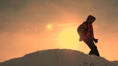 Turist parlak güneş ışınlarının karlı tepe üstünde duruyor. Gezgin dağlardan sarı günbatımı bir arka plan üzerine iner. insanlar zor koşullarda çalışmalarını.