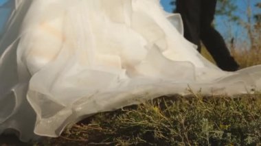 güzel bir beyaz gelin damat şehir dışında olan yol boyunca yürüyüş yakın çekim, elbise. İki kez mutlu aşıklar el ele tutuşarak yolda git. Sevgi ve sadakat aile kavramı.