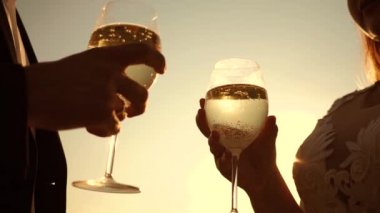 İki aşık ile köpüklü şarap şarap gözlük günbatımı arka plan üzerinde tutarak. portre. seven çift, takım çalışması. başarı ve zafer kutluyor. Şampanya parıldıyor ve güneşte köpükler. Ağır çekim