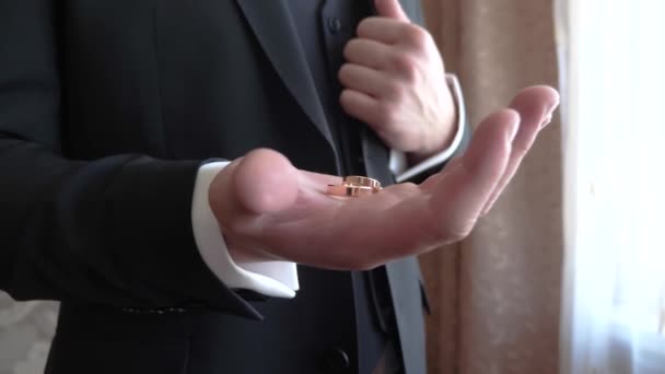 新郎は彼の手に金の結婚指輪を保持し、彼の上着のポケットに入れます。クローズ アップ。家族の休日のコンセプトです。彼は愛する女性のための金の宝石類. — ストック動画