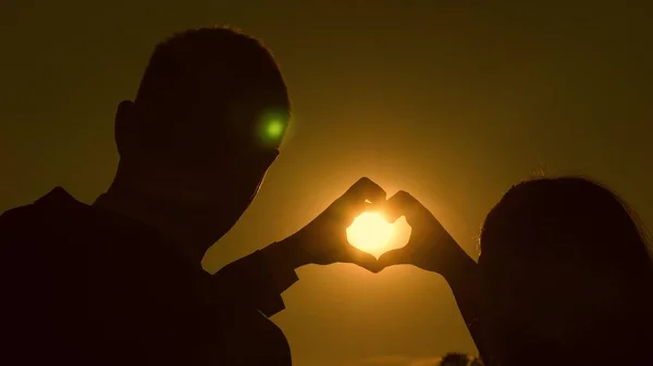 O sol está nas mãos. Uma menina e seu namorado fazendo uma forma de coração pelas mãos em frente a um belo pôr do sol no horizonte. trabalho de equipa de um casal amoroso. celebrar o sucesso e a vitória . — Fotografia de Stock