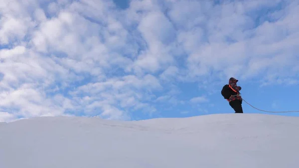 Альпинисты, связанные верёвкой, следуют друг за другом вдоль снежного хребта. Команда путешественников зимой поднимается на вершину горы. хорошо скоординированный командный туризм зимой — стоковое фото