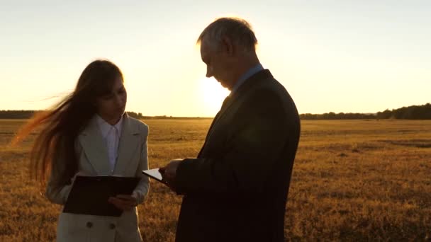 Trabajo en equipo hombres y mujeres en un proyecto empresarial. Reunión de negocios con hombres y mujeres en el parque. Empresario y empresaria con tableta negocian al atardecer y ríen . — Vídeos de Stock