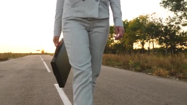 Zakenvrouw wandelingen op weg met een zwarte koffer in haar hand. Sensuele zakenvrouw met lange benen lopen op de weg. Close-up. — Stockvideo
