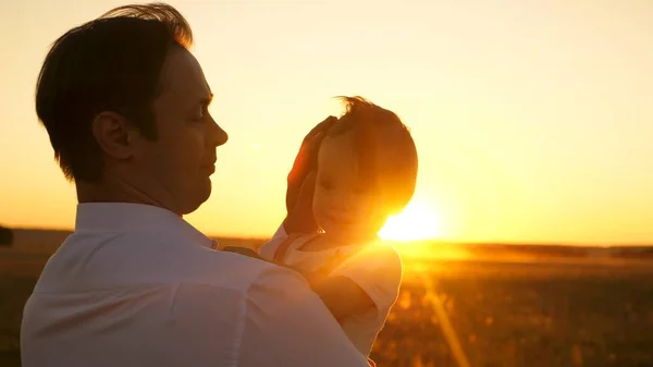 Happy dad holding small daughter in arms of the sun. Dad walks with baby in the meadow at sunset.